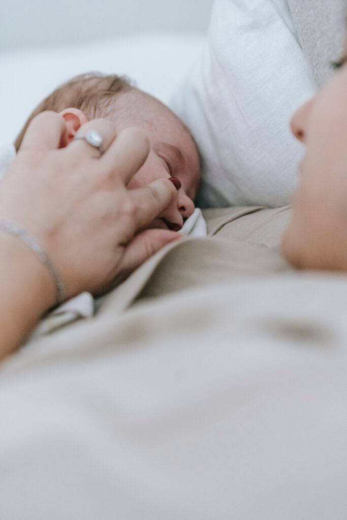 Schlafendes Neugeborenes im Arm der Mutter, eingewickelt in eine Decke.